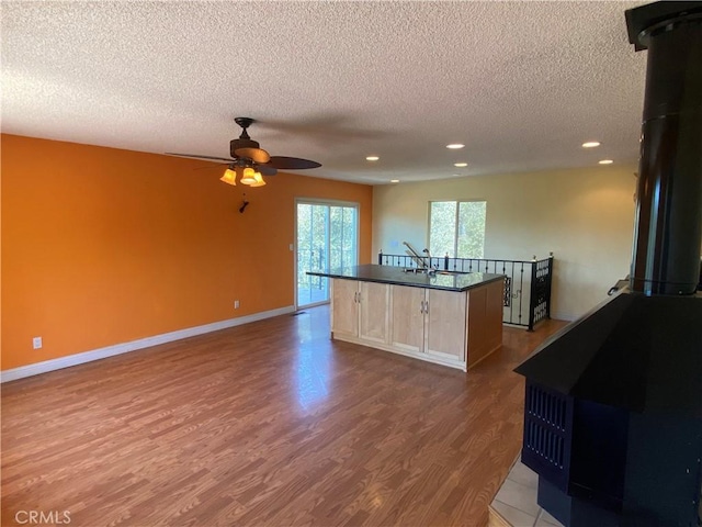 kitchen with light hardwood / wood-style flooring, ceiling fan, a textured ceiling, an island with sink, and light brown cabinetry