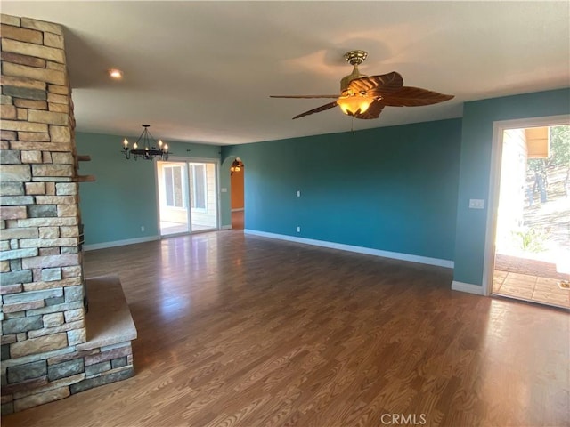 unfurnished living room with ceiling fan with notable chandelier and dark wood-type flooring