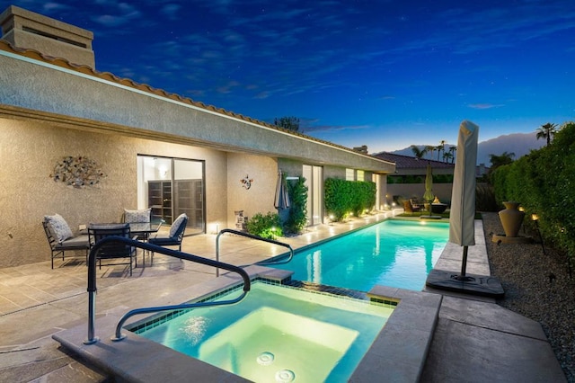 pool at dusk with an in ground hot tub and a patio