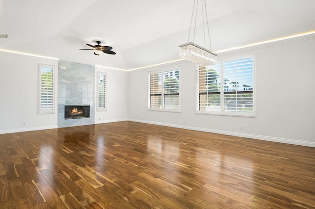 unfurnished living room featuring a wealth of natural light, a fireplace, ceiling fan with notable chandelier, and dark hardwood / wood-style floors