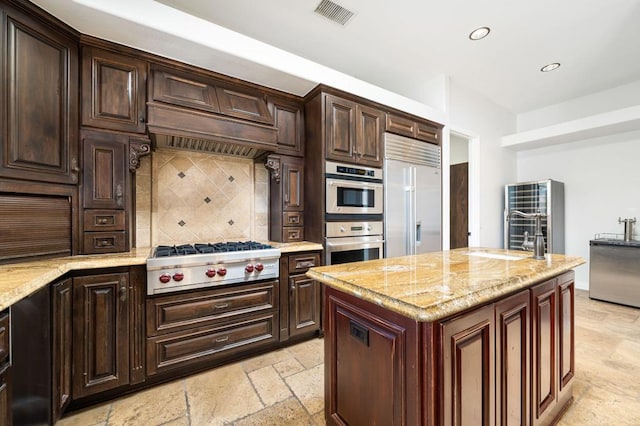 kitchen with tasteful backsplash, light stone countertops, a kitchen island, and stainless steel appliances