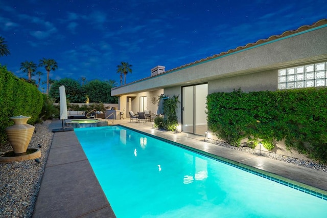 pool at night featuring an in ground hot tub and a patio