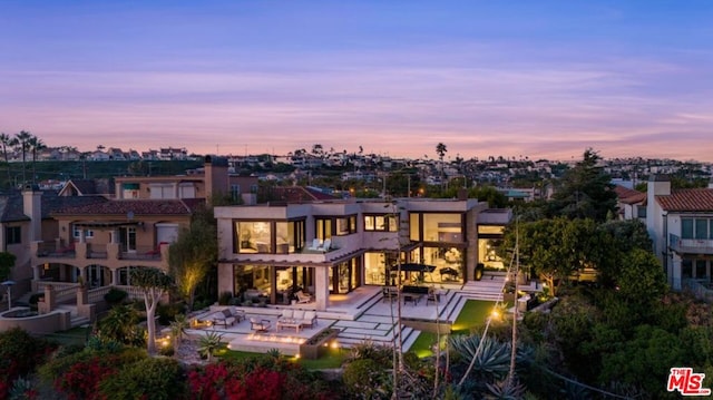 back house at dusk featuring a balcony and a patio area