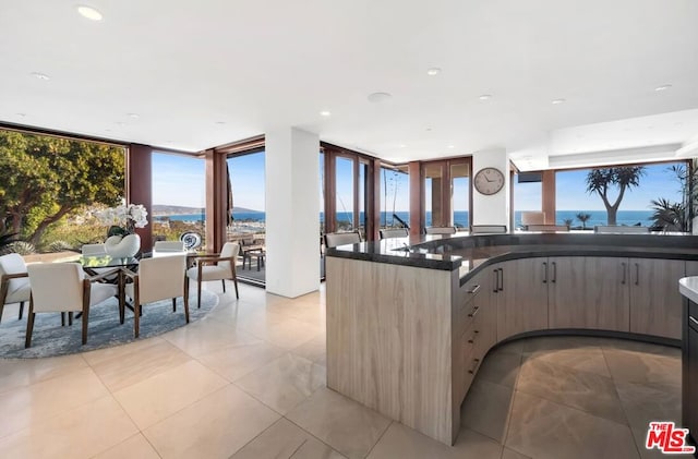 kitchen with floor to ceiling windows, light tile patterned floors, a water view, and a wealth of natural light