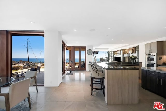 kitchen with a kitchen island, stainless steel double oven, a wall of windows, a kitchen bar, and a water view