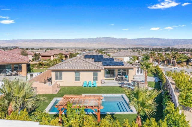 back of property featuring a mountain view, a fenced in pool, a patio area, a yard, and solar panels