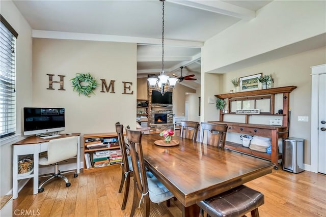 dining space with light wood-type flooring, ceiling fan with notable chandelier, a fireplace, and lofted ceiling with beams