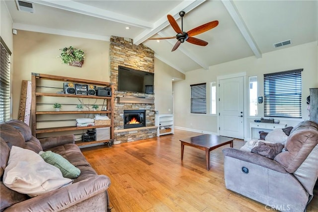 living room with light wood-type flooring, ceiling fan, vaulted ceiling with beams, and a stone fireplace