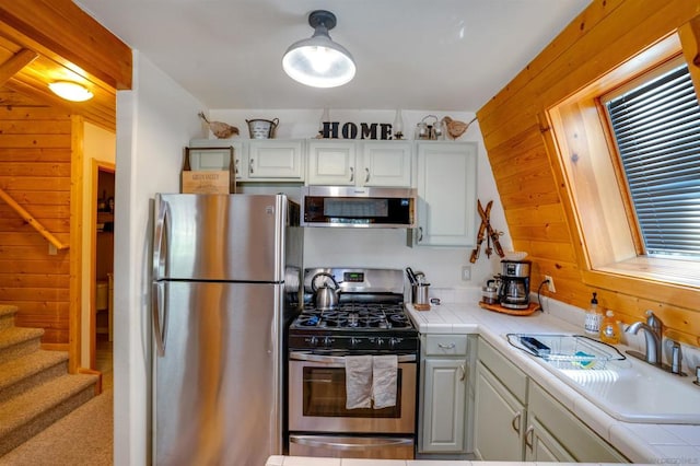 kitchen featuring stainless steel appliances, wood walls, tile countertops, and white cabinets