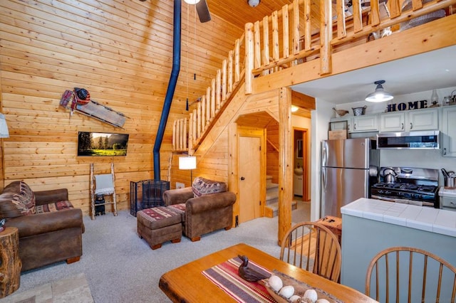 living room featuring light carpet, a high ceiling, wood walls, and ceiling fan