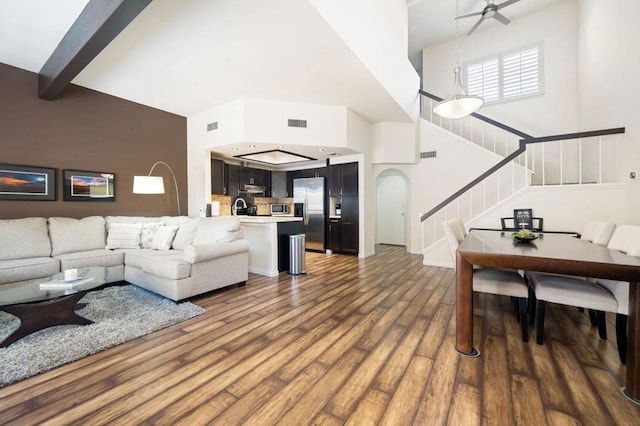 living room with hardwood / wood-style floors, a high ceiling, sink, ceiling fan, and beamed ceiling