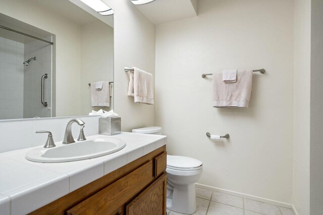 bathroom featuring tile patterned floors, vanity, a tile shower, and toilet