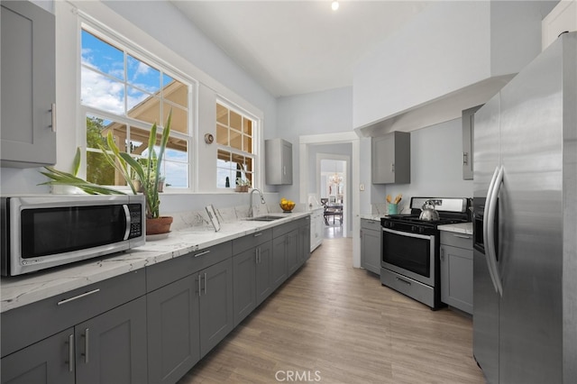 kitchen with light stone counters, sink, gray cabinetry, appliances with stainless steel finishes, and light wood-type flooring