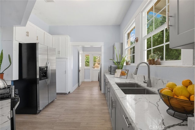 kitchen with light wood-type flooring, light stone counters, plenty of natural light, sink, and stainless steel fridge