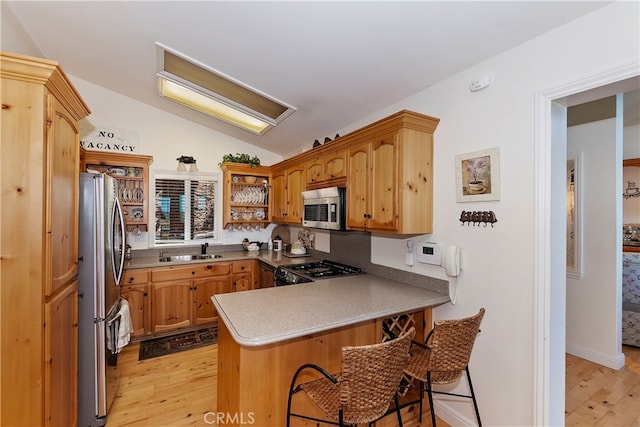 kitchen featuring appliances with stainless steel finishes, kitchen peninsula, light wood-type flooring, and lofted ceiling