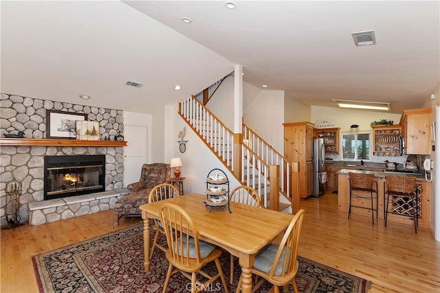 dining space with vaulted ceiling, light hardwood / wood-style floors, and a stone fireplace