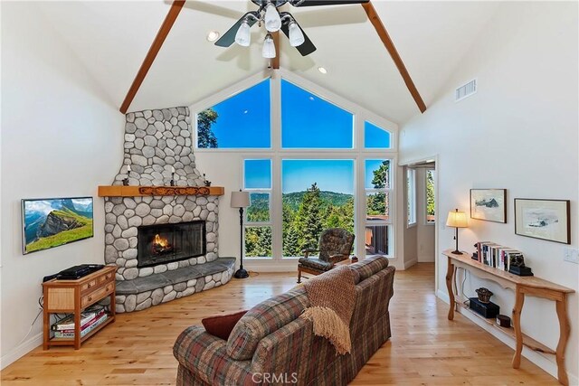 living room featuring high vaulted ceiling, light wood-type flooring, ceiling fan, and a stone fireplace