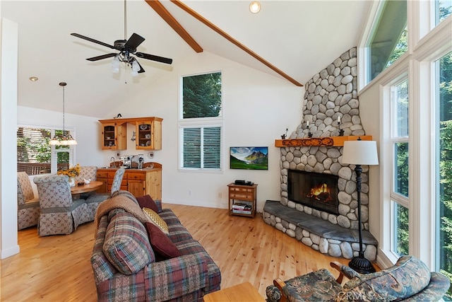 living room with light hardwood / wood-style flooring, ceiling fan, high vaulted ceiling, and a stone fireplace