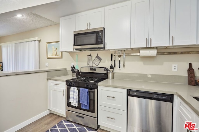 kitchen featuring appliances with stainless steel finishes, light wood-type flooring, a textured ceiling, and white cabinetry