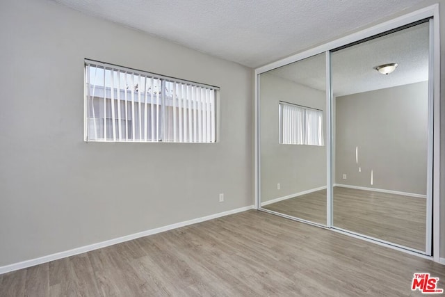 unfurnished bedroom with light hardwood / wood-style floors, a closet, and a textured ceiling