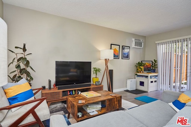 living room featuring an AC wall unit, wood-type flooring, and a textured ceiling