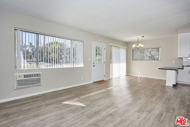 unfurnished living room featuring a notable chandelier, light hardwood / wood-style flooring, a textured ceiling, and an AC wall unit