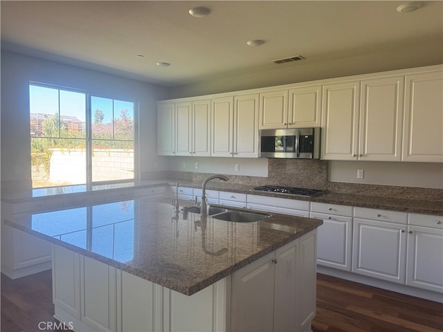 kitchen with white cabinetry, dark wood-type flooring, stainless steel appliances, a center island with sink, and sink