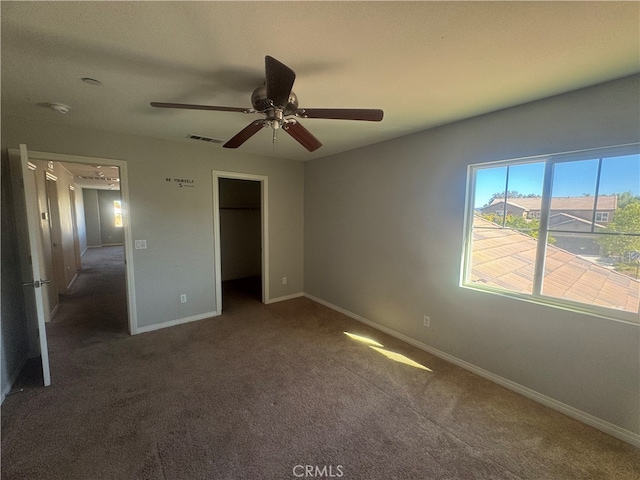 unfurnished bedroom with ceiling fan, a closet, dark colored carpet, and a spacious closet