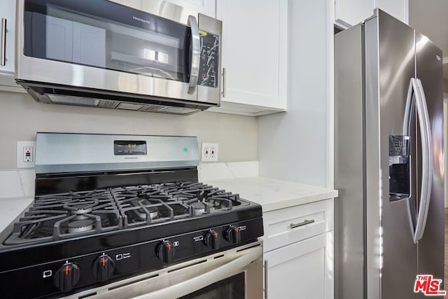 kitchen with light stone countertops, stainless steel appliances, and white cabinetry