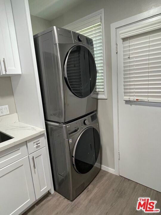 laundry room with stacked washer and clothes dryer, cabinets, and light wood-type flooring