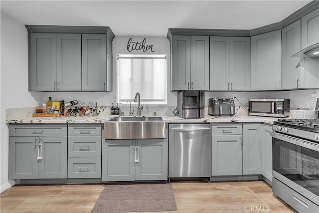 kitchen with appliances with stainless steel finishes, sink, light stone countertops, and light wood-type flooring