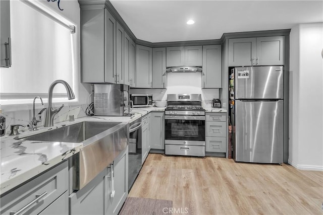 kitchen with stainless steel appliances, light hardwood / wood-style flooring, light stone countertops, range hood, and gray cabinets