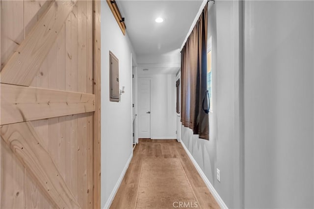 hallway featuring a barn door, electric panel, and light hardwood / wood-style flooring