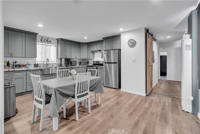 kitchen with sink, gray cabinets, a barn door, appliances with stainless steel finishes, and light hardwood / wood-style floors