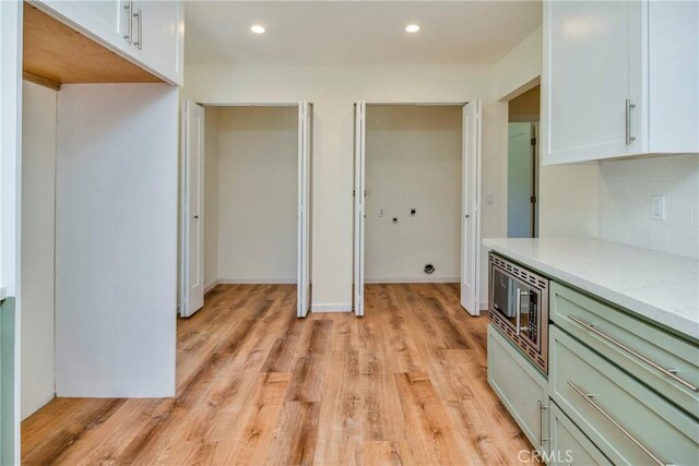 kitchen featuring backsplash, stainless steel microwave, light hardwood / wood-style flooring, and white cabinets