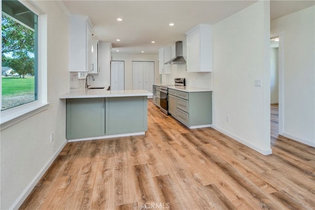 kitchen featuring stainless steel range with electric cooktop, a wealth of natural light, kitchen peninsula, and wall chimney range hood