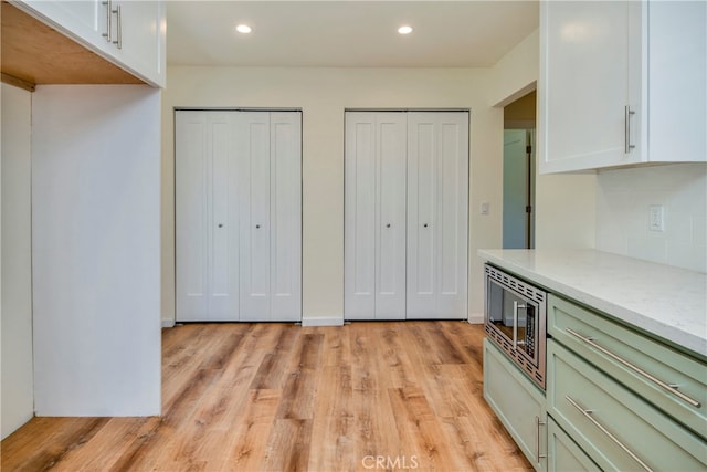 kitchen featuring light hardwood / wood-style flooring, white cabinetry, stainless steel microwave, and light stone counters