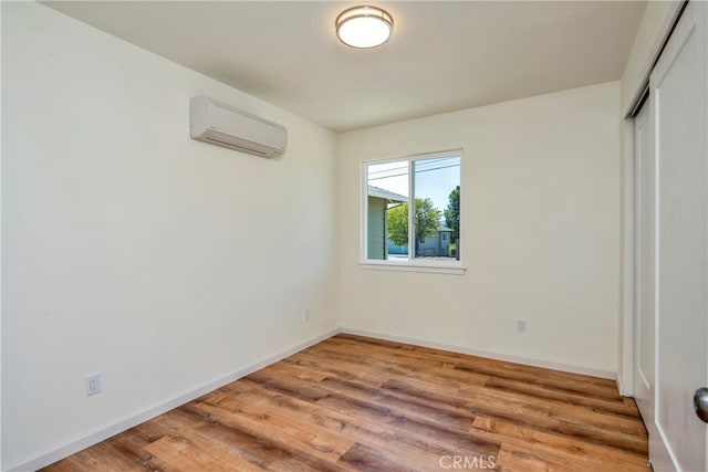 unfurnished bedroom with a closet, a wall unit AC, and hardwood / wood-style flooring