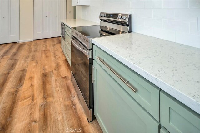 kitchen featuring light hardwood / wood-style flooring, green cabinets, electric stove, light stone countertops, and decorative backsplash