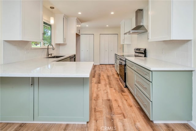 kitchen with appliances with stainless steel finishes, light hardwood / wood-style floors, pendant lighting, sink, and wall chimney range hood