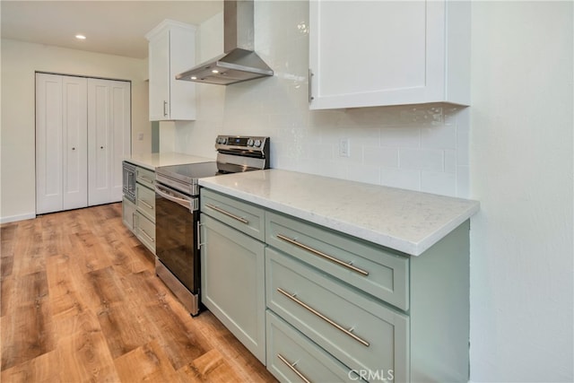 kitchen with wall chimney exhaust hood, light hardwood / wood-style flooring, backsplash, stainless steel electric stove, and light stone countertops