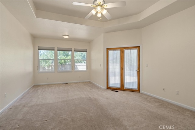 spare room with a raised ceiling, ceiling fan, light colored carpet, and french doors