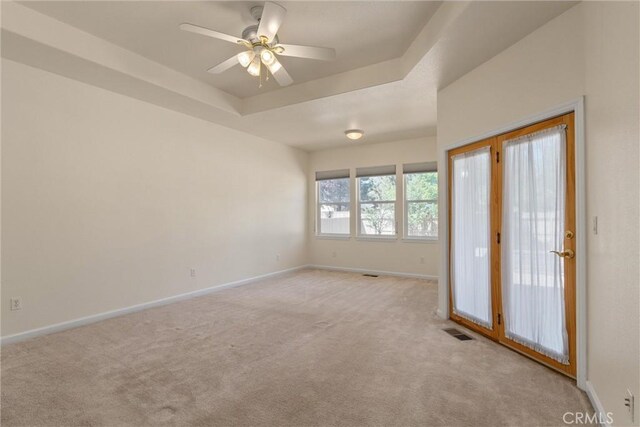 unfurnished room featuring a tray ceiling, light carpet, and ceiling fan