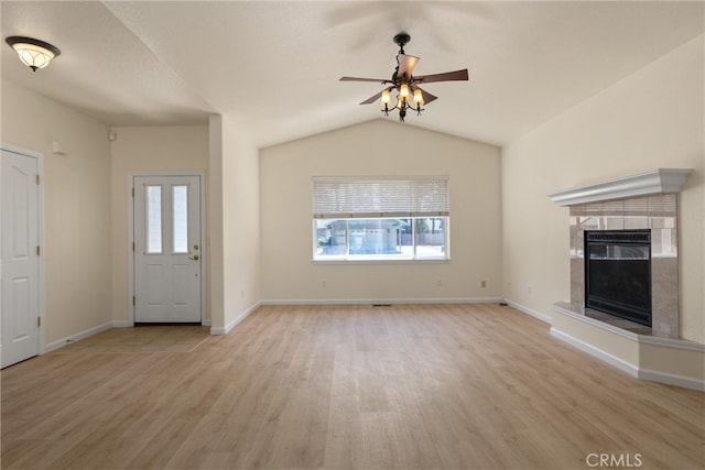 unfurnished living room with lofted ceiling, a tiled fireplace, ceiling fan, and light hardwood / wood-style flooring