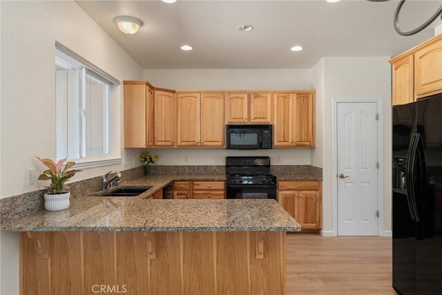 kitchen featuring kitchen peninsula, stone countertops, black appliances, light hardwood / wood-style flooring, and sink