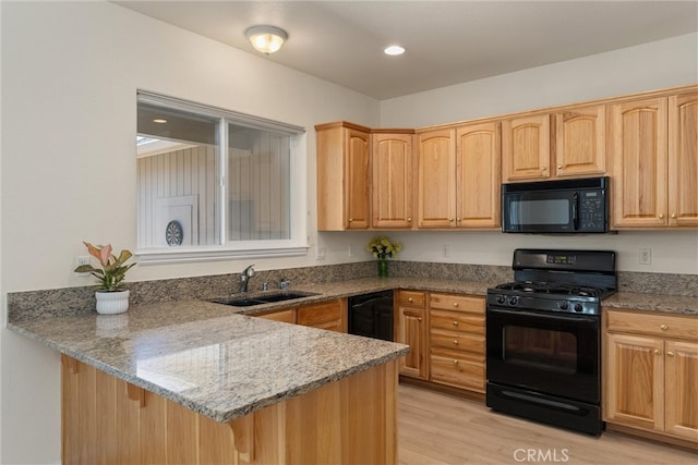 kitchen with light wood-type flooring, light stone counters, sink, kitchen peninsula, and black appliances