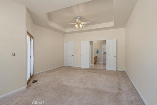 unfurnished bedroom featuring light carpet, ceiling fan, and a raised ceiling