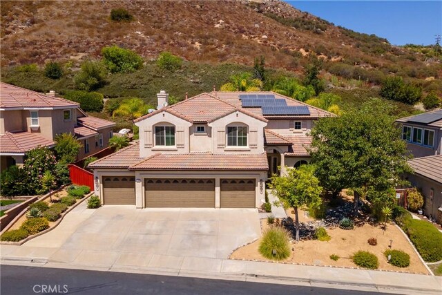 mediterranean / spanish-style house with a garage, a mountain view, and solar panels