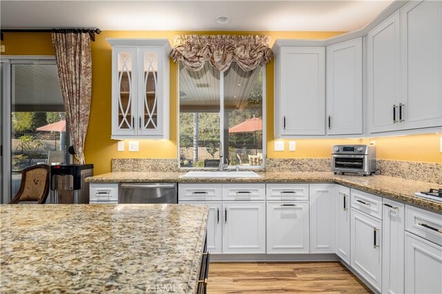 kitchen featuring light stone countertops, dishwasher, sink, and white cabinetry