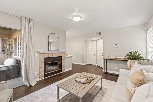 living room with a tiled fireplace, ceiling fan, and dark hardwood / wood-style flooring